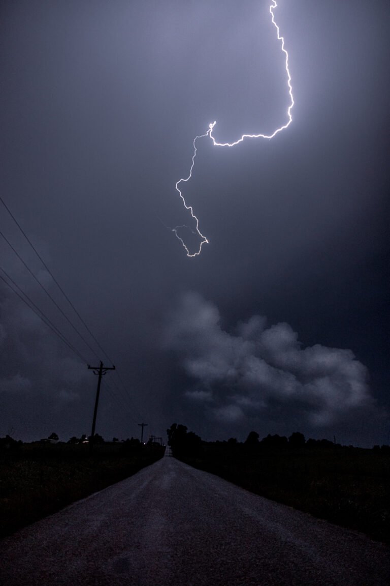 Lightning strikes the sky over a deserted rural road, viewed from a hilltop